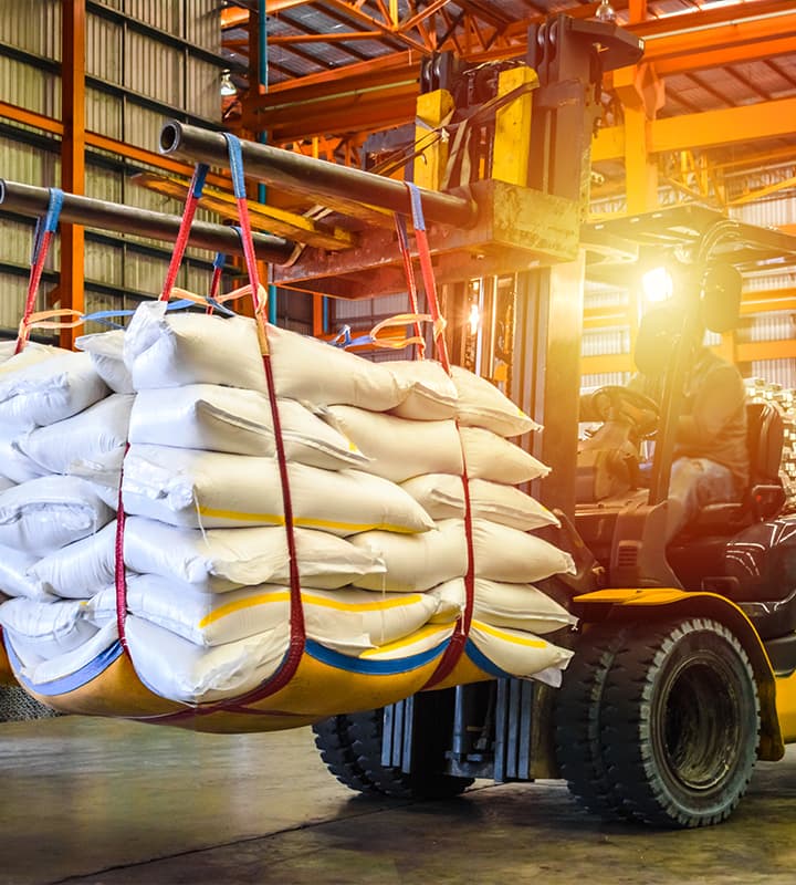 Forklift lifting white sacks inside a warehouse with warm lighting