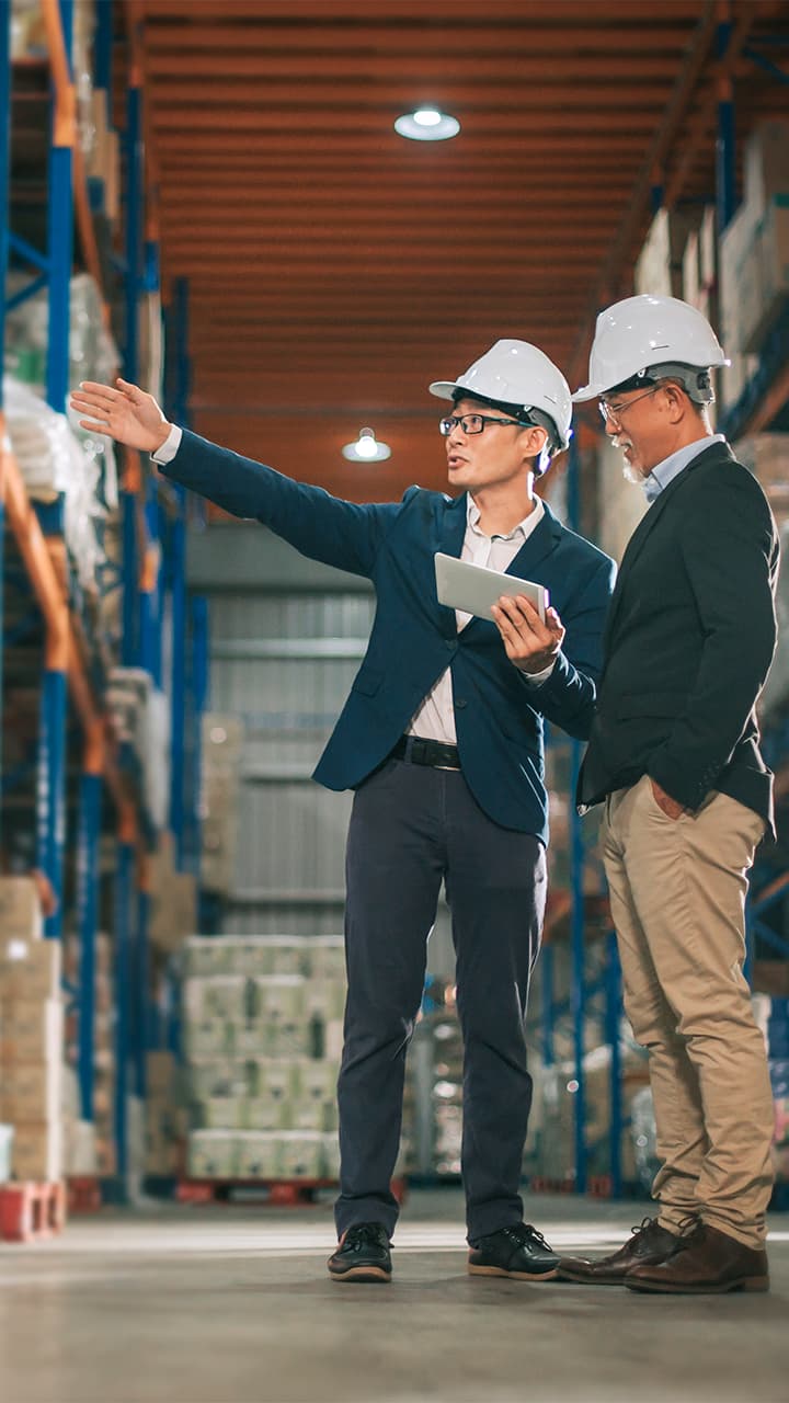 Two people wearing hardhats discussing inside a warehouse aisle